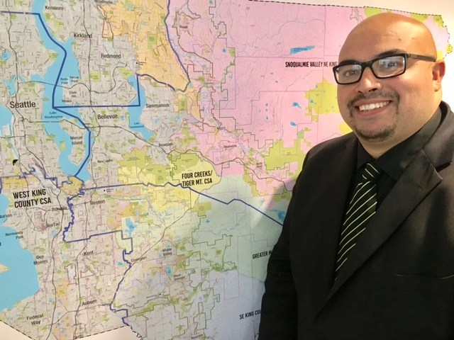 Hugo Garcia, King County Local Services' first Economic Development Program Manager, stands next to a map of King County.